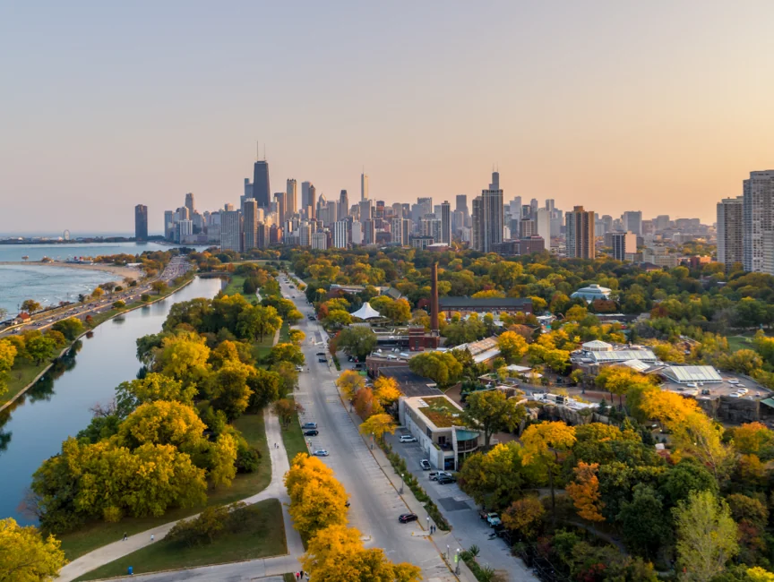 An aerial view of a city skyline at sunset, with a park filled with trees in autumn colors