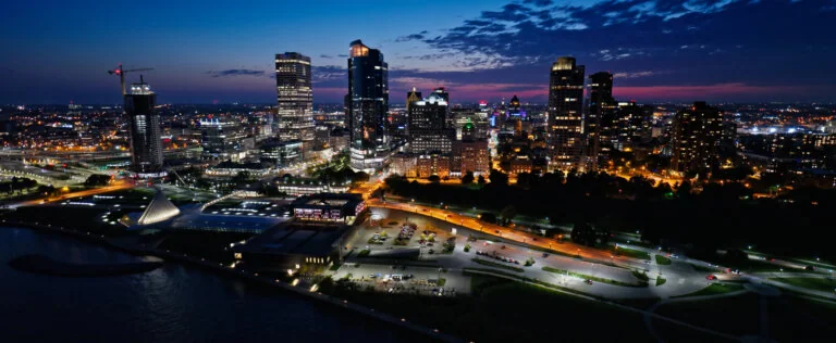 Aerial shot of East Town in Milwaukee, Wisconsin at nightfall on a Fall evening from over Lake Michigan, looking towards apartment buildings in Yankee Hill and the downtown office buildings of Juneau Town.